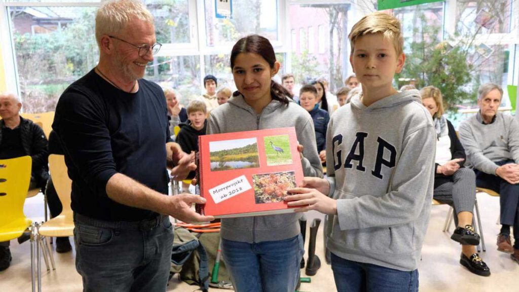 Nabu-Mitglied Jürgen Röper (von links) übergibt das sogenannte Entkusselungsbuch an Reem Aboud und Max-Ole Meyerdierks, die Stellvertreter der aktuellen siebten Jahrgänge an der Gesamtschule am Wällenberg.